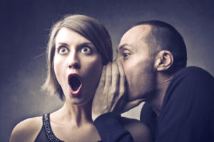 man gossiping into woman's ear