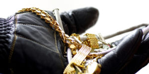 leather gloved hand holding small pile of gold jewellery